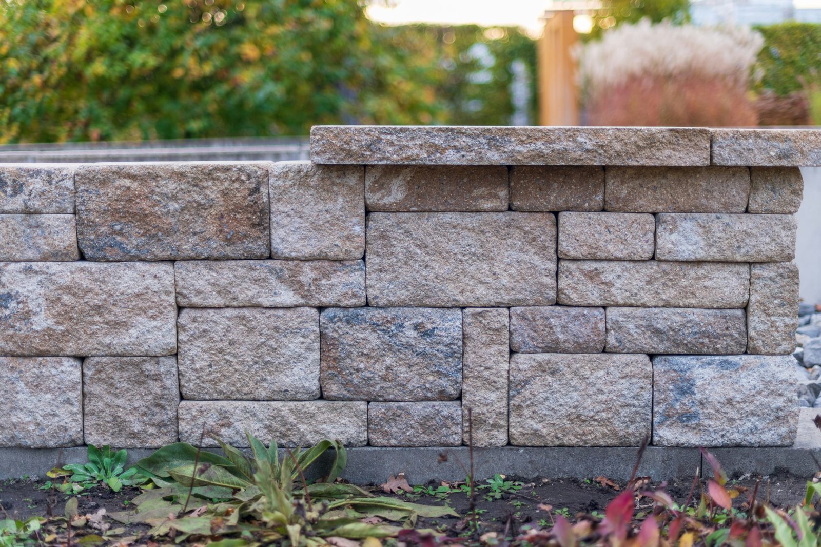 Stacked tumbled-block retaining wall with a stone cap and plants at its base