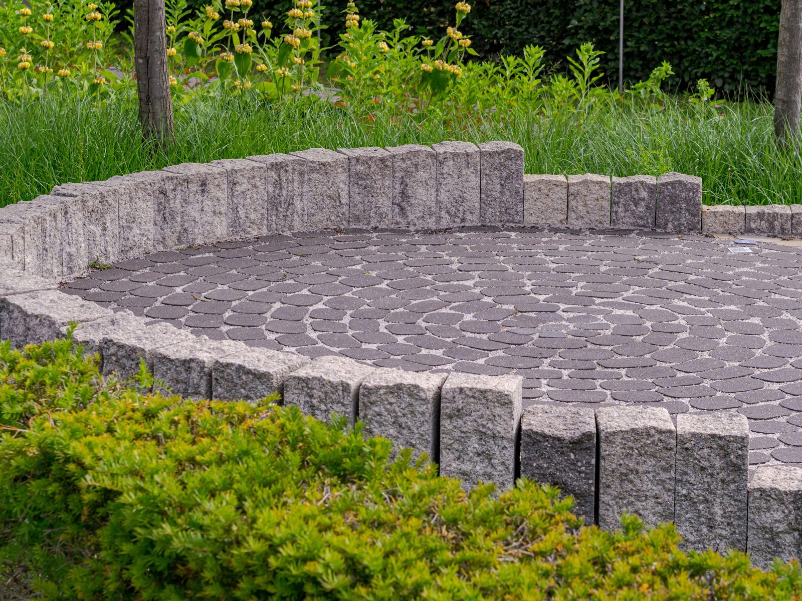 Round paver patio with a granite block border, surrounded by plantings