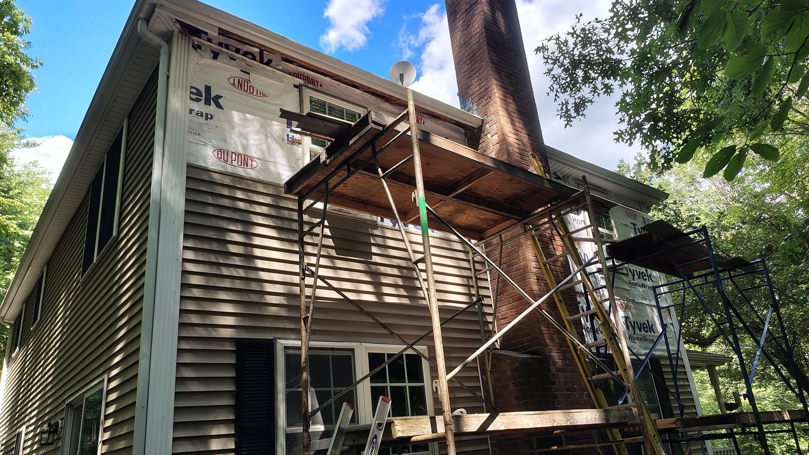 Two-story house with scaffolding at the chimney, new house wrap going on above the siding