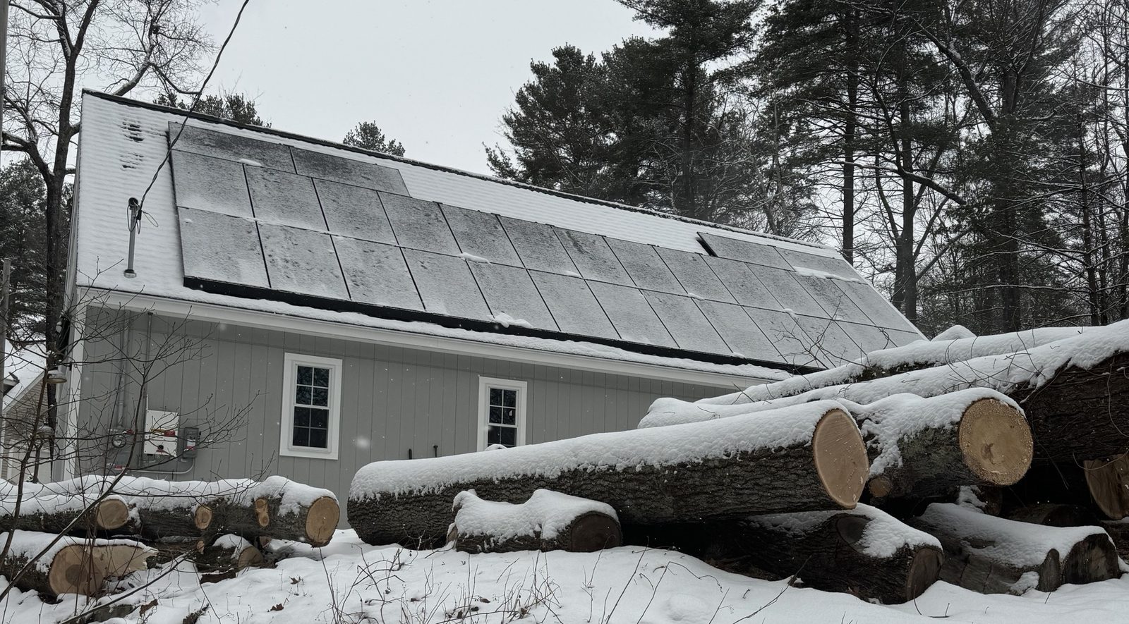 Solar array on a snow-dusted roof with pine trees behind