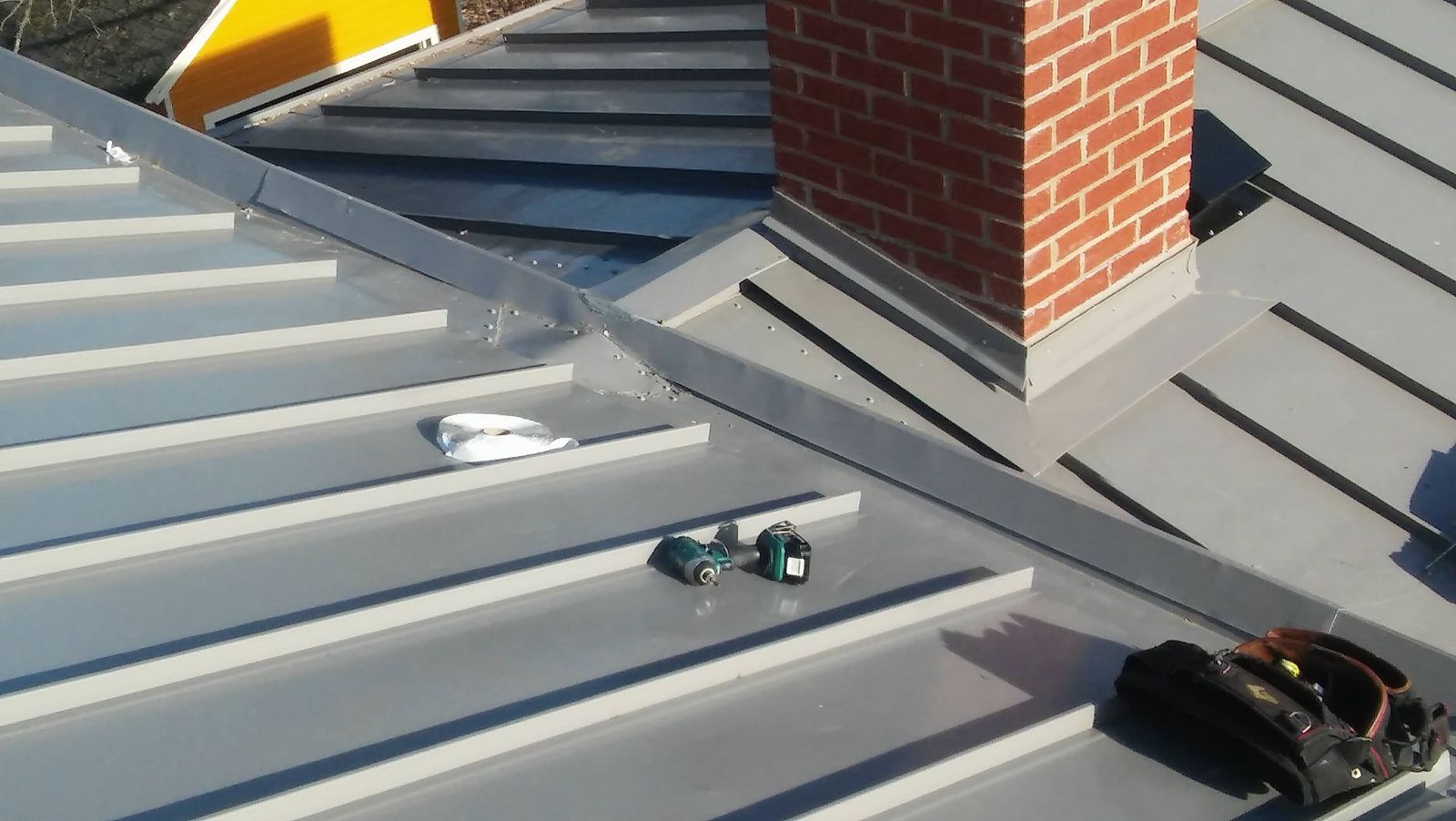 Gray standing-seam metal roof with flashing around a brick chimney