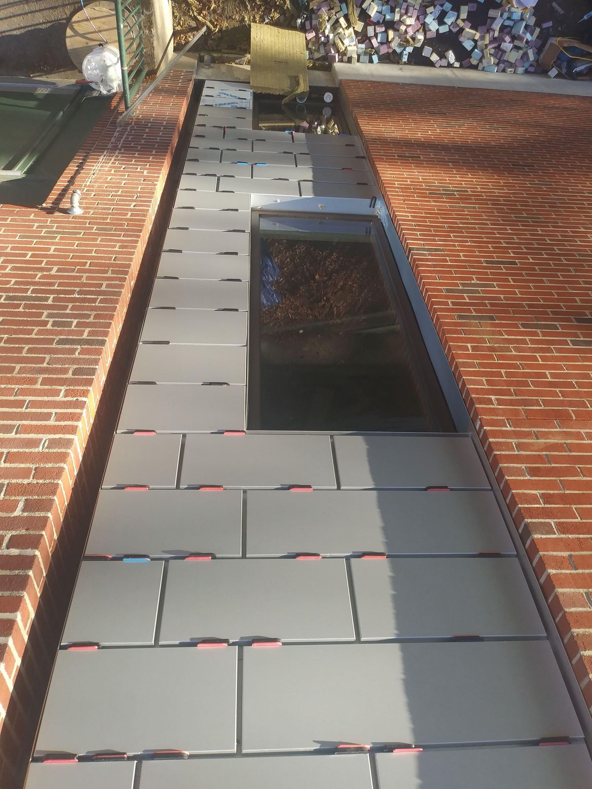 Gray metal wall panels being installed around a window between brick walls